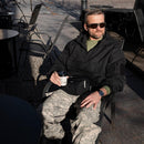 Man wearing black MIL-TEC German Military windproof fleece-lined hooded jacket sitting outdoors with coffee cup