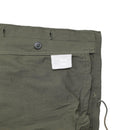 Close-up of olive green Genuine Greek military M65 field jacket fabric with button and white label inside.