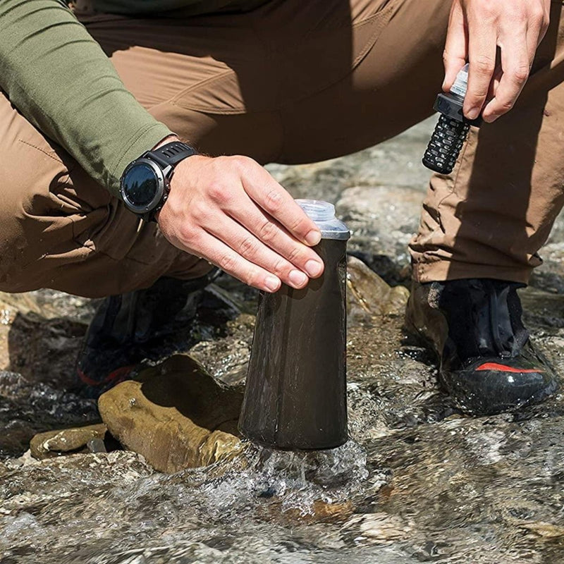Person filling a Katadyn BeFree Tactical 1.0L water filter bottle from a stream during outdoor adventure.