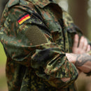 Close-up of a person wearing Leo Kohler tactical military shirt in flecktarn camouflage with German flag patch on sleeve