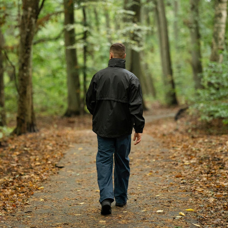 Man wearing black Mil-Tec waterproof rain jacket walking on forest trail with fall leaves on the ground