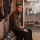 Man wearing an olive Austrian Army Alpine wool pullover sweater with high collar sitting indoors near military helmets and artifacts