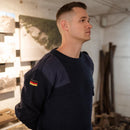 Man wearing navy blue German army pullover jumper with German flag patch on sleeve in indoor setting