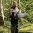 Man outdoors holding a rolled-up U.S. military Therm-A-Rest self-inflating lightweight sleeping pad in forest setting